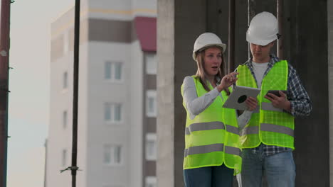 Construction-worker-man-and-architect-woman-in-a-helmet-discuss-the-plan-of-construction-of-house-tell-each-other-about-the-design-holding-a-tablet-look-at-the-drawings-background-of-sun-rays.